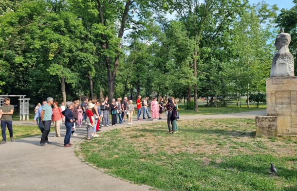 Tour group gathered in a sunny park near a stone statue on a pedestal.