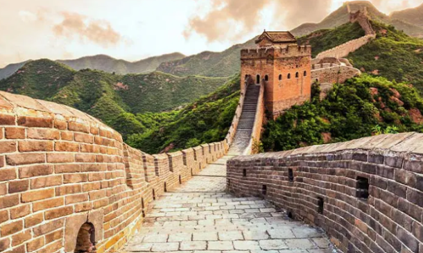 Section of the Great Wall of China with stone walkway and watchtower winding through green mountains.
