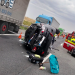 Upside-down car on a highway with emergency responders and a red ambulance nearby, cones marking the area.