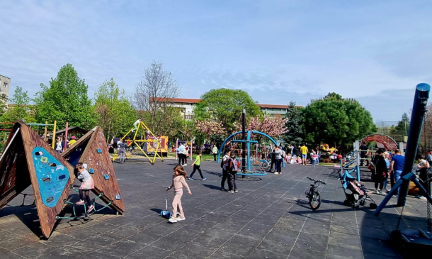 Wide view of a sunny public playground with wooden climbing frames and colorful play structures as children and adults explore.