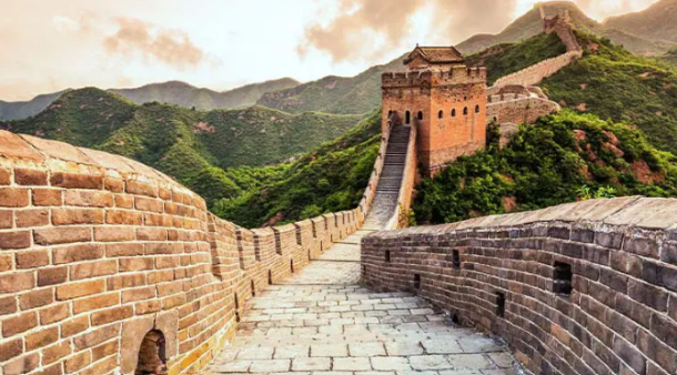 Section of the Great Wall of China with stone walkway and watchtower winding through green mountains.