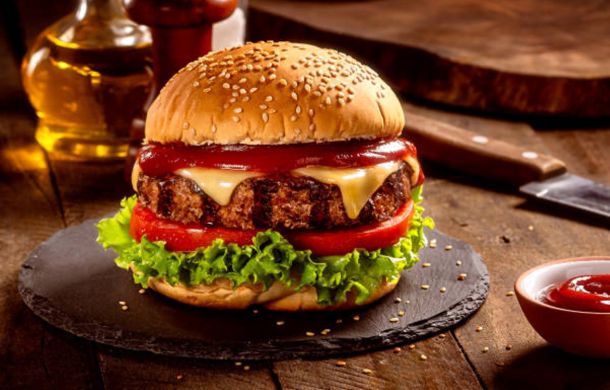 Juicy hamburger with sesame bun, melted cheese, beef patty, lettuce and tomato on a dark slate plate.