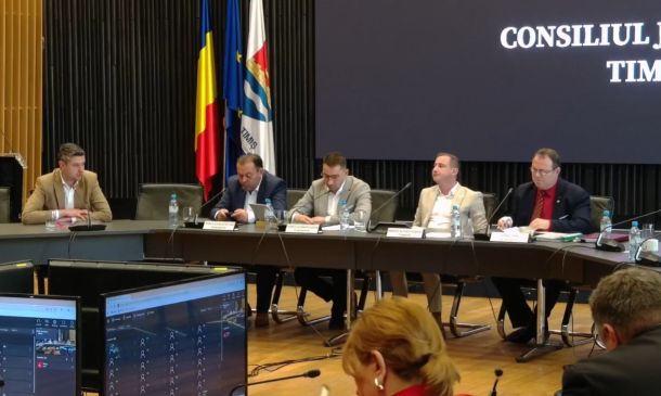 Five men sit at a long panel table in a council chamber, with flags behind and a large screen displaying 'CONSILIUL JUD TIMIȘ'.