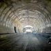Long concrete tunnel under construction; roadbed graded and workers gathered near the bright far end exit.