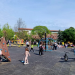Wide view of a sunny public playground with wooden climbing frames and colorful play structures as children and adults explore.