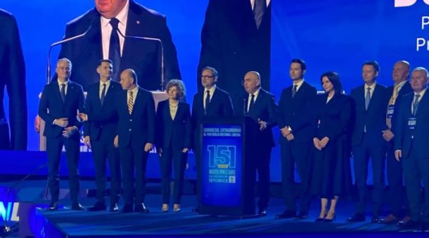 Group of formally dressed people on a stage at a conference, with a podium in the center.