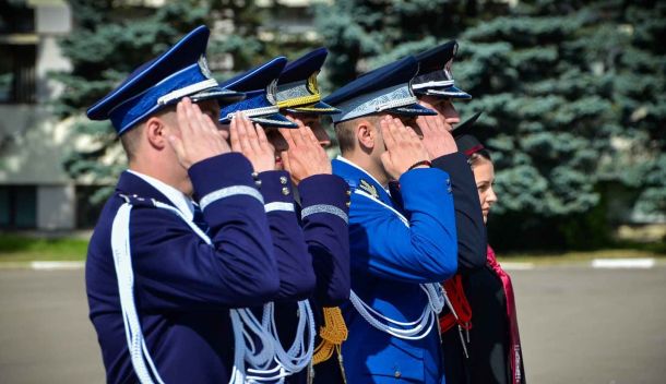 Group of uniformed officers saluting in a line outdoors during a ceremony.