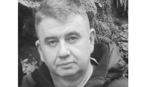 Black-and-white portrait of a middle-aged man with short hair wearing a dark jacket outdoors near rocks.