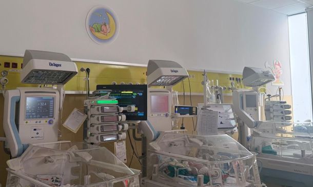 NICU room with several infant incubators and medical monitors mounted on a yellow wall panel.