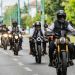 Group of motorcyclists riding down a city street, front rider wearing a black helmet and vest.