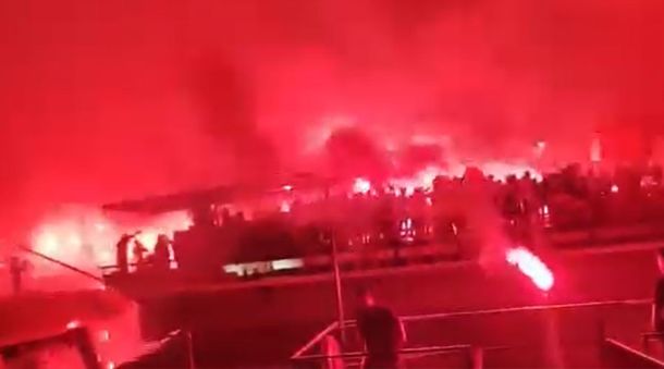 Crowd at night waving red flares, smoke lighting the scene in an intense red glow