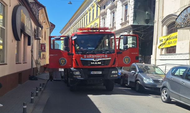 Red fire truck with open front doors blocking a narrow urban street; buildings line both sides and a yellow banner is visible on the right.