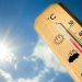 Wooden thermometer with a Celsius scale showing about 40°C, set against a bright blue sky with a shining sun.