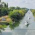 Boats cruising along a tree-lined canal with calm, reflective water viewed from above.