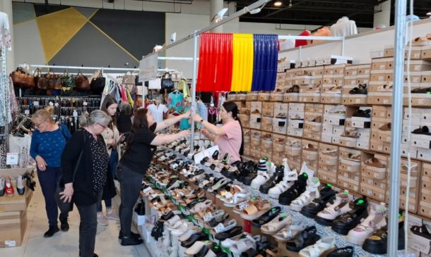 Shoppers browse a busy shoe stall inside a store; rows of sandals and sneakers line the displays with stacked shoeboxes in the background.