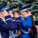 Group of uniformed officers saluting in a line outdoors during a ceremony.