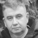 Black-and-white portrait of a middle-aged man with short hair wearing a dark jacket outdoors near rocks.