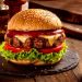 Juicy hamburger with sesame bun, melted cheese, beef patty, lettuce and tomato on a dark slate plate.