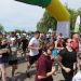 Group of runners starting a road race under a yellow inflatable arch, bib numbers visible on their shirts.